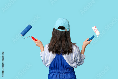 Female Asian painter with rollers on blue background, back view