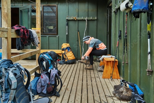 Bild auf Leinwand Woman putting on hiking shoes in front of a wooden cabin on a trail