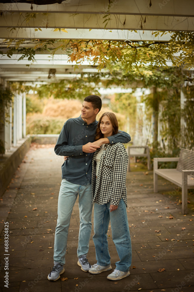 Fototapeta premium Young Cute Female Hugs Boyfriend. In Autumn Outdoor. Lovers Walking in Park. Attractive Funny Couple. Lovestory in Forest. Man and Woman. Cute Lovers in the Park. Family Concept. Happy Couple.