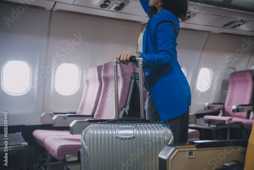 Asian female traveler putting luggage into overhead locker on airplane during boarding.