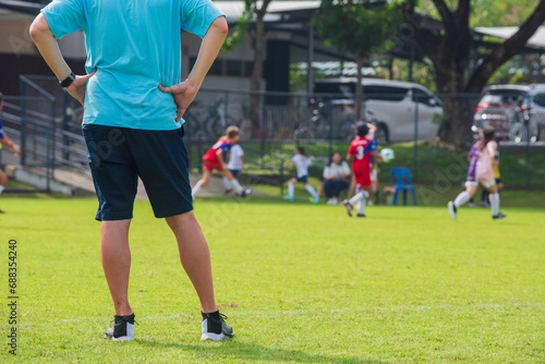 Dad standing and watching his son playing football in a school tournament on a sideline with a sunny day. Sport, outdoor active, lifestyle, happy family and soccer mom and soccer dad concept. © athichoke.pim