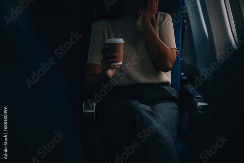 Asian woman enjoying enjoys a coffee comfortable flight while sitting in the airplane cabin  Passengers near the window.