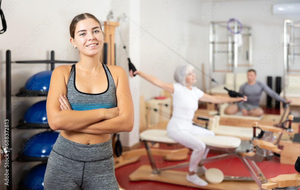 Smiling girl after pleasant Pilates workout is standing in fitness room. Advertising poster for coaching services, gym, fitness activity