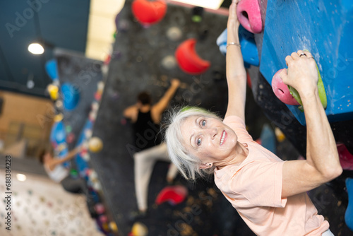 Senior woman without safety rope climbs dark bouldering wall in gym. active longevity concept