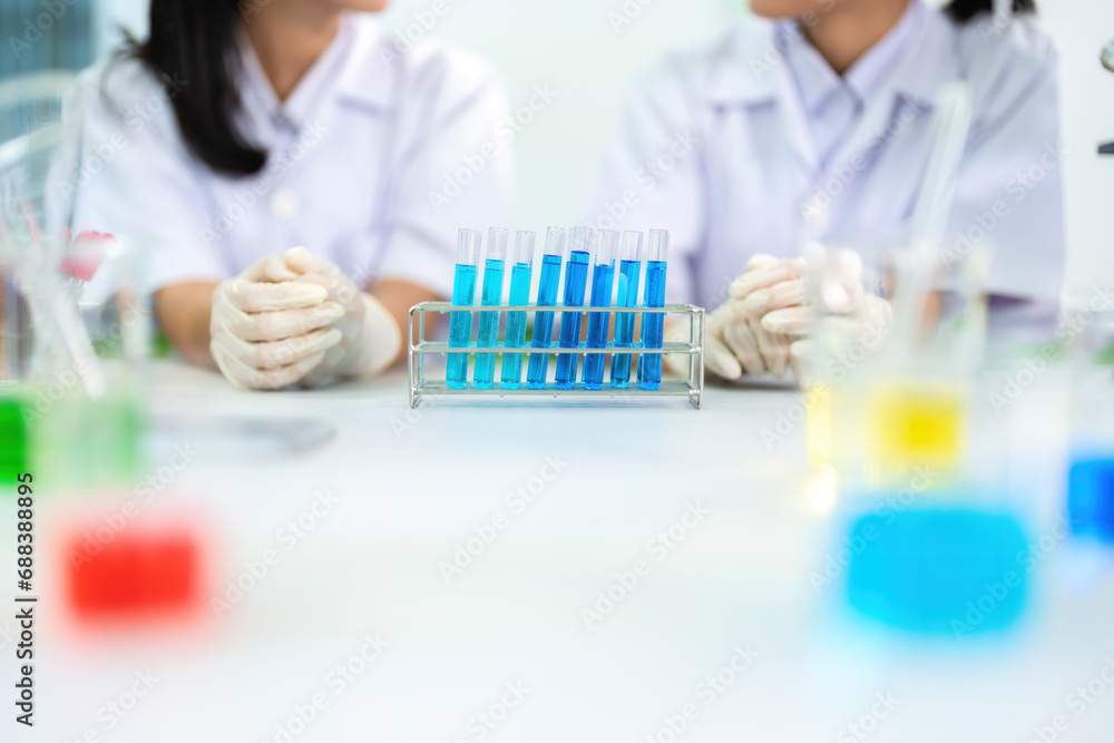 Fototapeta premium Half-body view of scientists talking with several research and experimental glass tubes containing a blue chemical solution. To produce biological medicine in the future for use in treating diseases.