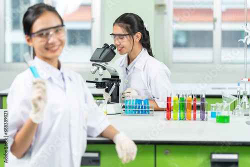 Two Asian female scientists are students. Looking through a microscope and holding a chemical test tube in a lab There is equipment for testing biology  glass tubes  pickers for medical work.