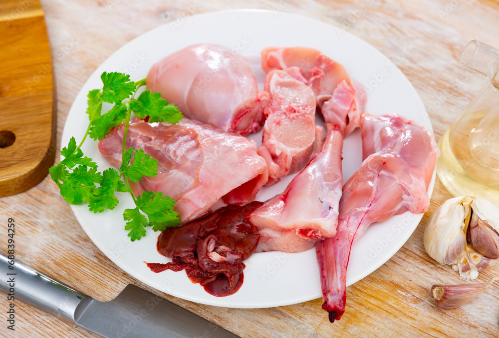 Chopped fresh raw rabbit on plate with greens, garlic and spices prepared for cooking on table. Healthy dietary food