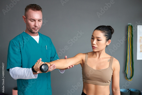 Foto Physiotherapist telling patient to keep arm straight when doing exercise with du