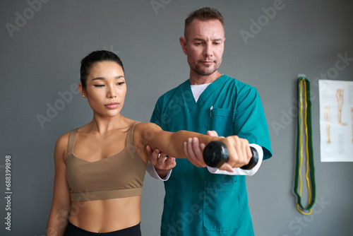 Foto Rehab nurse helping sportswoman to do exercise with dumbbell when recovering fro