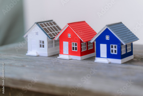 A small red house model with a red roof sits next to a pile of coins on a wooden surface.