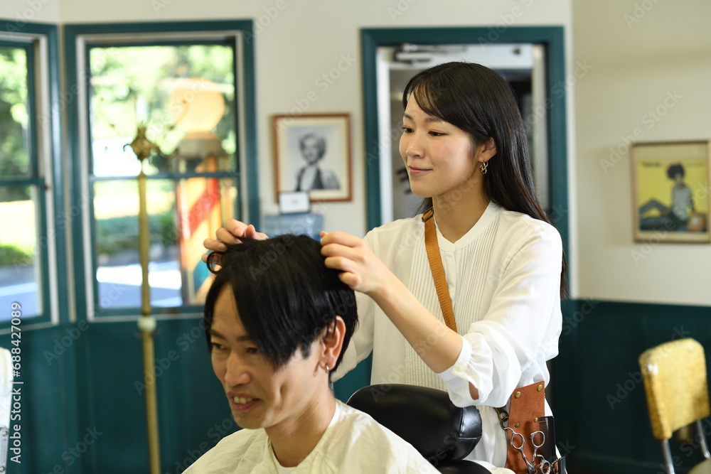 男性客のヘアスタイリングをするアジア人の女性美容師 男性客のヘアスタイリングをするアジア人の女性美容師