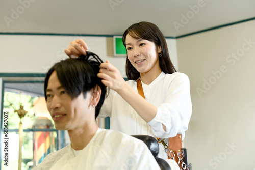 男性客のヘアスタイリングをするアジア人の女性美容師