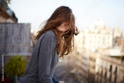 funny portrait of a young white and brunette woman with her hair covering her face during a windy day in Barcelona photo