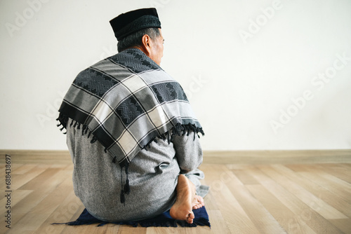 Asian Muslim man praying at mosque gesturing last movement of salat reciting salam to the right then to the left. photo