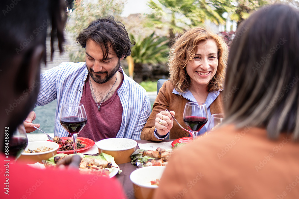 A group of friends share food and wine outdoors, enjoying time and engaging in cheerful conversation.