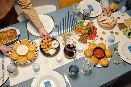 Above view of unrecognizable man and woman putting homemade snack on table served with tasty treats prepared for Hanukkah dinner photo