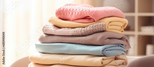 Freshly washed and neatly folded women's clothes stacked on bedroom dresser, featuring a variety of pastel colored sweaters. Close-up shot with copy space.
