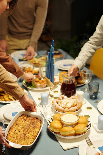 Hands of Jewish family members putting cutlery with appetizing homemade food on table served for Hanukkah dinner