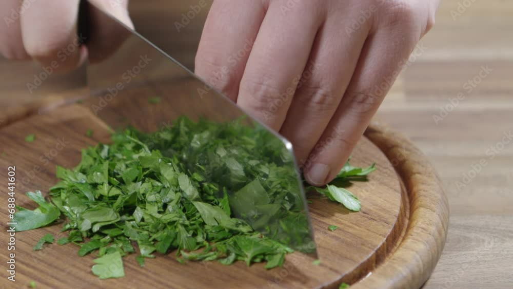 Chopping parsley with a very sharp knife on a wooden board, a basic ingredient of chimichurri Chopping parsley with a very sharp knife on a wooden board, a basic ingredient of chimichurri