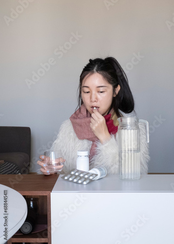 Asian girl taking medicines  pills  supplements at home  in winter clothing and scarf  flu  cold