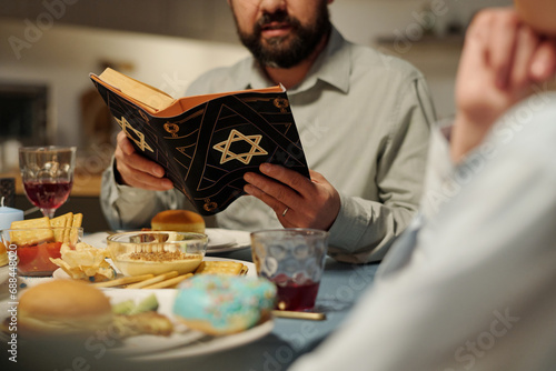 Cropped shot of bearded man with open Torah reading Psalms or other verses from Old Testament while sitting by served table photo