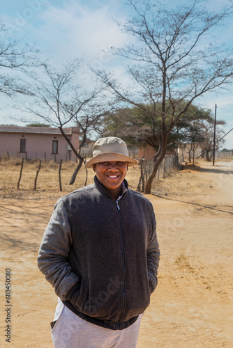 Slika na platnu villager , happy overweight young african man with a hat walking on a dirt road