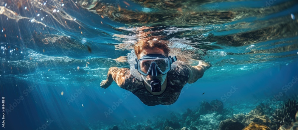 Unrecognizable male diver in snorkeling gear swimming underwater in deep blue sea.
