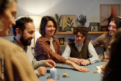 Young smiling woman putting coin on center of table while betting during leisure game with members of her family after Hanukkah dinner photo