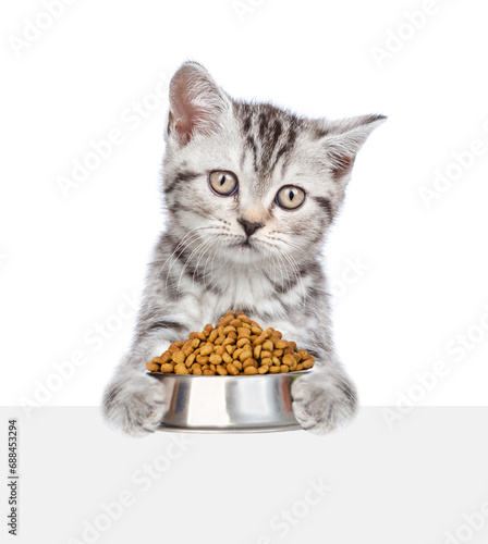 Cat holding bowl of dry food and looking above empty white banner. isolated on white background