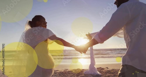 Animation of light spots over african american couple getting married on beach photo