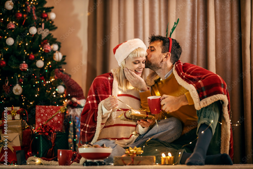 A happy couple is exchanging gifts and kissing on christmas eve and new year at home.