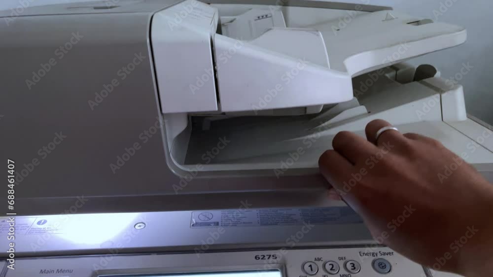 A person's hand closes the photocopier cover to photocopy a file A person's hand closes the photocopier cover to photocopy a file