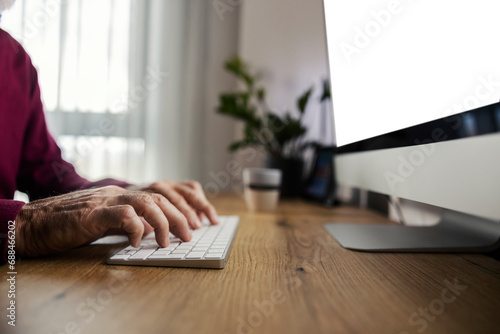 Close up of a senior's hands typing on a keyboard at home office.