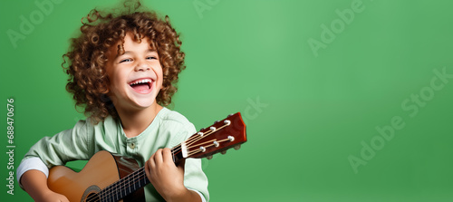 Joyful kid playing guitar, green background and copy space, banner for music school