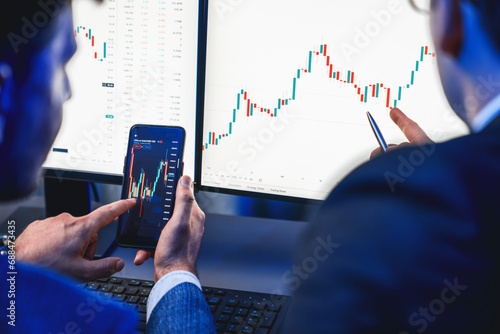 Two stock exchange traders researching data on smartphone and laptop screen server of dynamic digital currency. Investors analyzing market stock at decorative neon blue-light of workplace. Sellable.