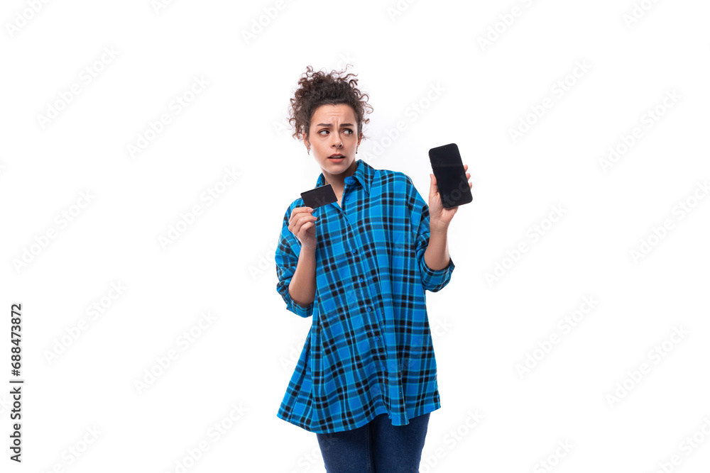 young curly european woman dressed informally in a blue plaid shirt holding a plastic card and smartphone young curly european woman dressed informally in a blue plaid shirt holding a plastic card and smartphone