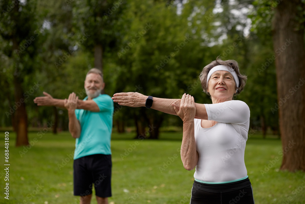 Senior couple doing warm-up exercises during physical therapy class on nature Senior couple doing warm-up exercises during physical therapy class on nature