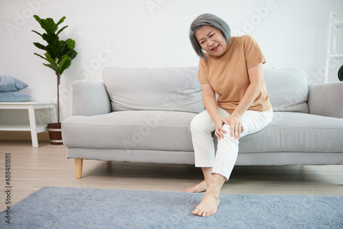 senior woman suffering from knee ache on sofa photo