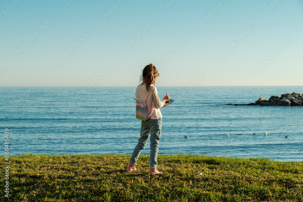 Playa de Pedregalejo, Málaga, niña seis años en el césped, frente al mar, escribiendo en su diario, día soleado, cielo sin nubes Playa de Pedregalejo, Málaga, niña seis años en el césped, frente al mar, escribiendo en su diario, día soleado, cielo sin nubes