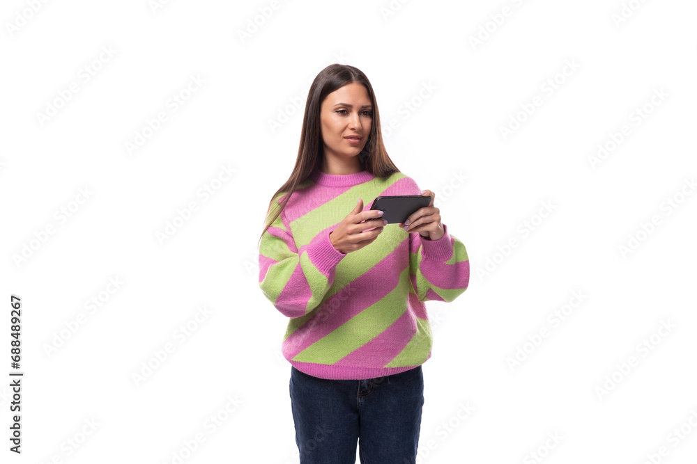 e-business concept. 35 year old feminine model woman dressed in pink and green pullover watches video on smartphone e-business concept. 35 year old feminine model woman dressed in pink and green pullover watches video on smartphone
