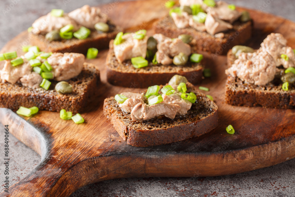 Tasty sandwiches with cod liver, capers and green onion close-up on a wooden board on the table. Horizontal Tasty sandwiches with cod liver, capers and green onion close-up on a wooden board on the table. Horizontal