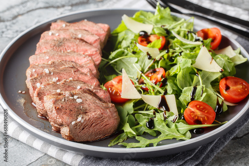 Sliced Seared Steak Tagliata di Manzo served with arugula, cherry tomatoes and parmesan close-up in a plate on the table. Horizontal
