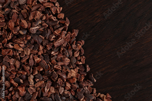 Unsweetened Organic Cacao Nibs on brown wooden surface, top view. Crunchy pieces of peeled, crushed and lightly roasted cocoa beans. Natural Sugar-free product