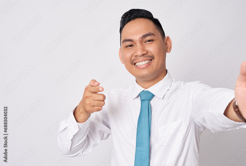 Close up smiling happy fun young Asian businessman wearing a formal shirt tie and pointing finger on camera isolated on white background. Taking a selfie shot on the phone Close up smiling happy fun young Asian businessman wearing a formal shirt tie and pointing finger on camera isolated on white background. Taking a selfie shot on the phone