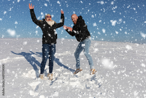 Ein verliebtes Paar bestehend aus Mann und Frau springen voller Freude im Schnee in die Luft und zeigen ihre Freude durchs Lachen und Lächeln photo