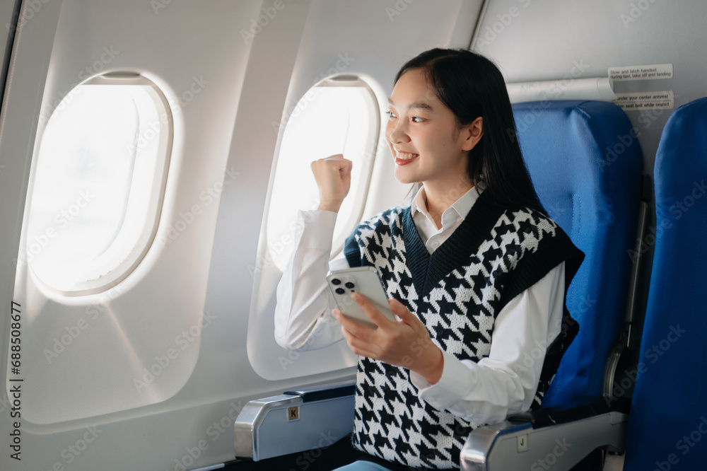 Fototapeta premium Attractive Asian female passenger of airplane sitting in comfortable seat while working laptop and tablet with mock up area using wireless connection.