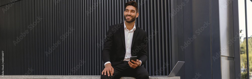 Businessman with mobile phone sitting on bench on office building background. High quality photo Businessman with mobile phone sitting on bench on office building background. High quality photo
