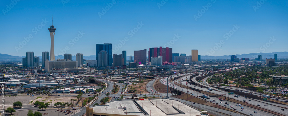Aerial view of Las Vegas skyline featuring the Stratosphere Tower, iconic hotels, and mountains, under a clear blue sky with busy highways, capturing the city's dynamic essence.