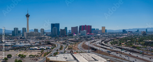 Aerial view of Las Vegas skyline featuring the Stratosphere Tower  iconic hotels  and mountains  under a clear blue sky with busy highways  capturing the city s dynamic essence.