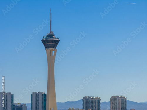Elevated angle view of the modern Stratosphere Tower in Las Vegas, Nevada, amidst high-rise buildings under a clear blue sky, with distant mountains and no visible people.